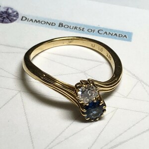 Pu&ograve; includere: Un anello d'oro con un diamante e uno zaffiro incastonati in una fascia attorcigliata. L'anello &egrave; contrassegnato da "18K" e "925".
