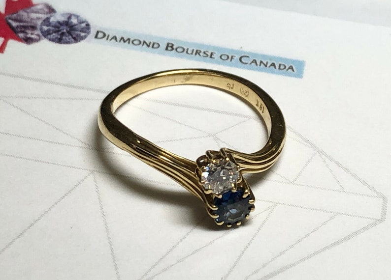 Pu&ograve; includere: Un anello d'oro con un diamante e uno zaffiro incastonati in una fascia attorcigliata. L'anello &egrave; contrassegnato da "18K" e "925".