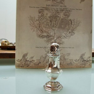 Puede incluir: Azucarero de plata con tapa perforada y base redonda. El azucarero está sobre una superficie blanca delante de un documento antiguo con el texto "IMPORTANT SILVER" y "From the estates of Mollie Carvan, New York, Ernest S. Morrison, New Jersey".