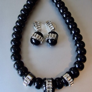 May include: A black and silver necklace and earrings set. The necklace is made of black beads and has silver accents. The earrings are silver with black beads and rhinestones.