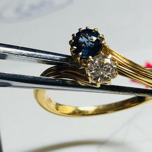 Pu&ograve; includere: Un anello d'oro con uno zaffiro blu e un diamante. L'anello &egrave; incastonato in una fascia attorcigliata.