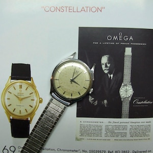 Könnte beinhalten: Eine vintage Omega Constellation Chronometer Armbanduhr mit weißem Zifferblatt und schwarzen Zeigern. Die Uhr ist an einem silbernen Metallband. Das Bild zeigt auch eine Schwarzweißanzeige für die Omega Constellation Uhr.