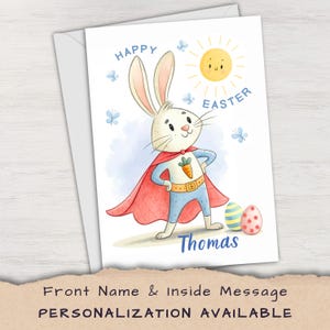 May include: Easter greeting card featuring a superhero bunny with a red cape and blue suit. The card has a smiling sun, butterflies, and the words "Happy Easter." Two decorated Easter eggs and the name "Thomas" are also visible.
