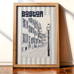 May include: Framed art print featuring a black and white illustration of a Boston street scene. The word "BOSTON" is printed in bold, stylized letters at the top. The print is set against a light blue and white striped background.