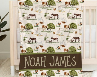May include: A personalized baby blanket with a farm animal print. The blanket features cows, chickens, donkeys, and trees on a cream background. The name "NOAH JAMES" is printed in brown letters on a green and brown stripe.