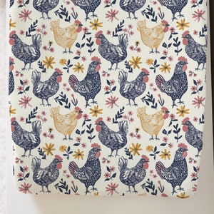 May include: A white fabric with a repeating pattern of black and yellow chickens and pink and yellow flowers.