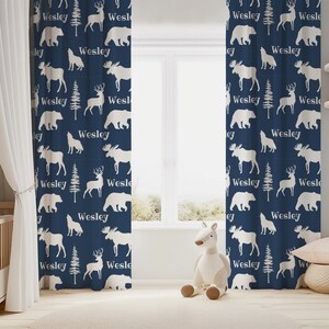 May include: A pair of navy blue curtains with a white silhouette pattern of moose, deer, bears, and trees. The pattern repeats throughout the curtains and includes the name "Wesley" in white text.