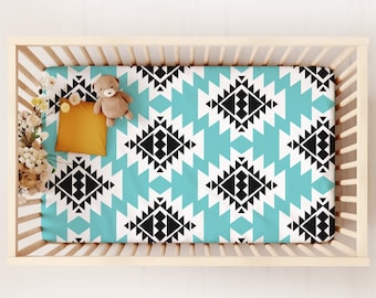 May include: A turquoise and black geometric patterned fitted crib sheet. The sheet is in a crib with a stuffed animal and a yellow pillow.