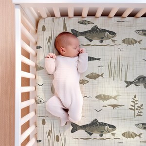 May include: A baby sleeping in a crib with a white crib sheet featuring a brown and white fish pattern.