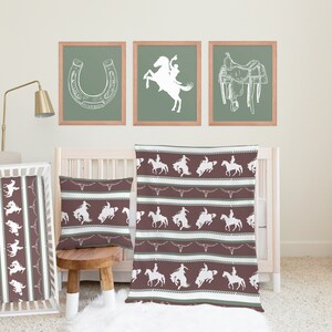 May include: A brown and green baby crib bedding set with a cowboy theme. The set includes a crib sheet, a blanket, and a pillow. The bedding features a white silhouette of a cowboy riding a horse.