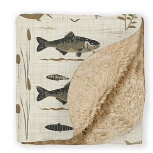 May include: A soft, beige fleece throw blanket with a cream-colored printed side featuring a pattern of brown fish and reeds.