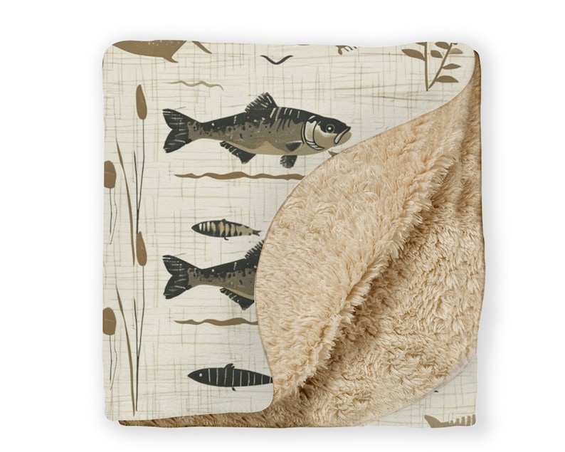 May include: A soft, beige fleece throw blanket with a cream-colored printed side featuring a pattern of brown fish and reeds.
