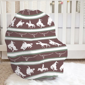 May include: A brown and white patterned baby chair cover with a design of cowboys riding horses and longhorns.