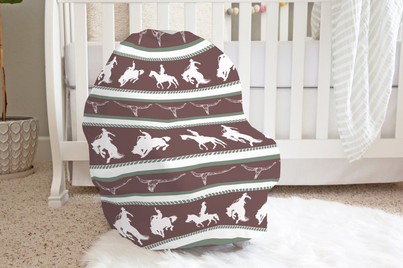 May include: A brown and white patterned baby chair cover with a design of cowboys riding horses and longhorns.