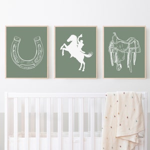 May include: Three framed prints with a green background and white illustrations of a horseshoe, a cowboy riding a horse, and a saddle.