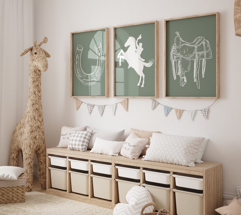 May include: A light wood bench with six white storage bins. The bench is decorated with a string of white and blue pennant flags. Three pillows are on the bench, one with a white and black checkered pattern, one with a white and gray chevron pattern, and one with a white polka dot pattern. Three framed prints are on the wall behind the bench. The prints are on a sage green background and feature white line drawings of a horseshoe, a cowboy riding a horse, and a saddle.