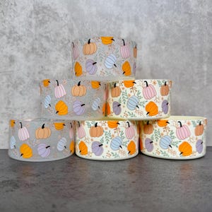 May include: Six ceramic bowls with a repeating pattern of colorful pumpkins and floral accents. The pumpkins are in shades of orange, pink, blue, and purple. The bowls are stacked on top of each other.