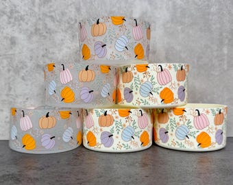 May include: Six ceramic bowls with a repeating pattern of colorful pumpkins and floral accents. The pumpkins are in shades of orange, pink, blue, and purple. The bowls are stacked on top of each other.