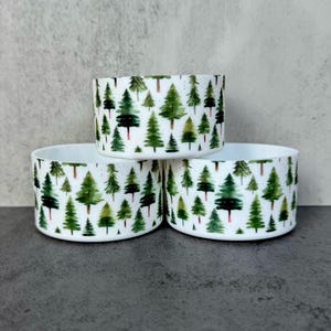 May include: Three white ceramic bowls with a forest scene design. The bowls are stacked on top of each other. The design features green trees on a white background.
