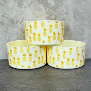 May include: Three white ceramic bowls with a pineapple pattern. The bowls are stacked on top of each other.