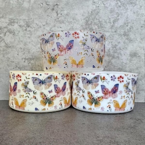 May include: Three white ceramic bowls with a butterfly pattern. The bowls are stacked on top of each other. The butterflies are in shades of pink, purple, blue, and yellow. The bowls have a white background with a floral pattern.