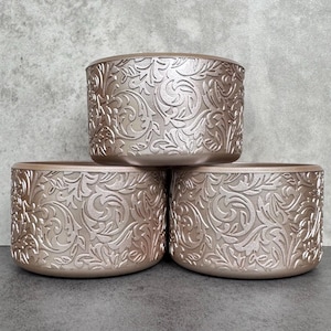 May include: Three round, decorative planters with a metallic gold finish. The planters have a raised, embossed floral pattern.