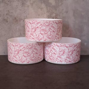 May include: Three white ceramic bowls with a pink floral pattern. The bowls are stacked on top of each other.