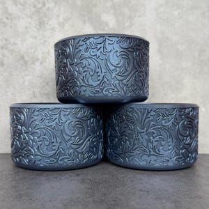 May include: Three gray ceramic planters with a raised floral pattern. The planters are stacked on top of each other.