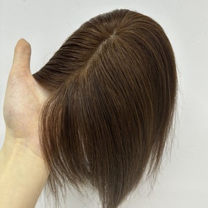 May include: A brown human hair topper with a natural-looking parting. The topper is designed to add volume and coverage to thinning hair.