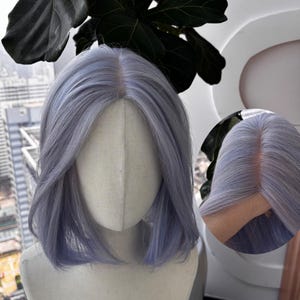 May include: A light purple bob wig on a mannequin head. The wig has a natural-looking parting and a gentle wave. The hair is a soft, pastel shade of purple, with a smooth, shiny texture. The wig is styled to fall just below the shoulders.