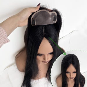 May include: A black hair topper with a lace base and clips is held above a mannequin head with long, black hair. The topper is designed to add volume and coverage. A smaller inset image shows the hair topper in place.