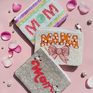May include: Three beaded pouches with the words "MOM" and "MAMA" in pink and orange, and a silver pouch with the word "Mom" in red. The pouches have zipper closures and are decorated with pearls and a bow.