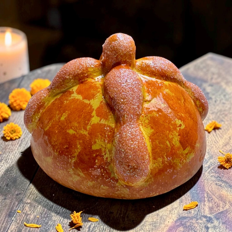 May include: A round, golden-brown pan de muerto bread featuring a central knob and four radiating bone-shaped dough strips on top. The surface is glazed and lightly dusted with sugar, showcasing a mottled yellow and brown baked crust texture.