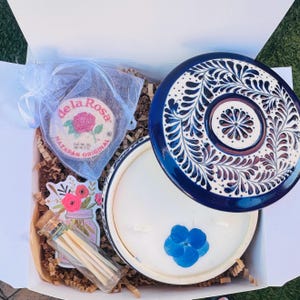 May include: A gift box containing a blue and white ceramic candle with a floral design, a small jar of matches, and a mazapan candy. The candle has a blue floral design and a matching lid. The mazapan candy is in a small mesh bag.