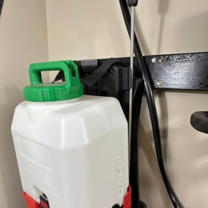 May include: A red and black Milwaukee backpack sprayer with a white 4-gallon tank and a green handle. The sprayer is hanging on a wall.