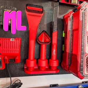 May include: Three red and black vacuum cleaner attachments with a brush, crevice tool, and upholstery tool. The attachments are mounted on a red wall mount with the text "Milwaukee" on the crevice tool.
