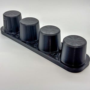 May include: A black plastic organizer with four round, black, textured knobs. The knobs are arranged in a row on the organizer.