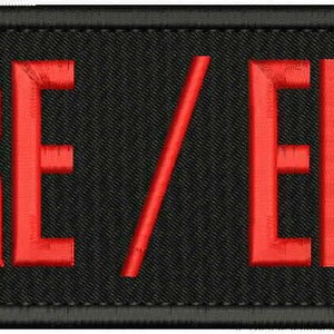 May include: A rectangular black embroidered patch with a thick black border. The text FIRE / EMT is stitched in bold, bright red capital letters across the center of the patch. The fabric has a visible textured weave throughout the black background.