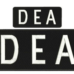 May include: Two rectangular black embroidered patches featuring the white text DEA in a bold, sans-serif font. The patches have a stitched border and a textured fabric surface, with one patch being significantly larger than the other.