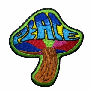 May include: An embroidered patch shaped like a mushroom with a black border. The cap features the word PEACE in blue letters against a yellow background, with red, pink, and blue radial segments below. The stem is brown with dark brown stitching.