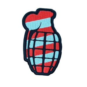 May include: An embroidered patch shaped like a hand grenade featuring a diagonal striped pattern of bright red and light blue. The design is outlined with a thick dark navy blue border and includes a black grid pattern over the grenade body.