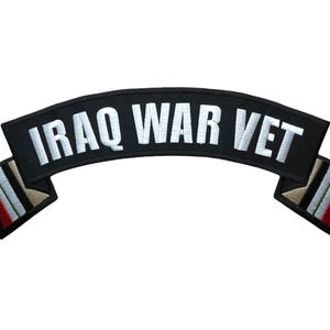 May include: A curved black embroidered patch featuring the white text IRAQ WAR VET. The patch has a banner-style design with decorative ends displaying vertical stripes in red, white, black, and tan colors, finished with a black border.