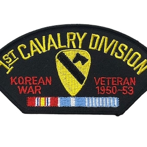 May include: A black embroidered patch shaped like a crest with yellow text reading 1ST CAVALRY DIVISION. It features a yellow shield with a black diagonal stripe and horse head, red text KOREAN WAR VETERAN 1950-53, and a multi-colored ribbon bar.