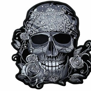May include: A black and silver embroidered patch featuring a skull wearing a paisley bandana, surrounded by detailed roses. The design includes small embedded rhinestones throughout the embroidery, set against a solid black background.