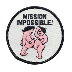 May include: A circular embroidered patch with a white background and a black stitched border. The patch features the black text MISSION IMPOSSIBLE! above two stylized pink figures with black hair, depicted in a cartoon style on a white fabric base.