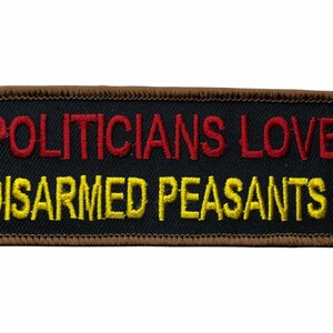 May include: A rectangular embroidered patch with a black background and a brown stitched border. The text POLITICIANS LOVE is embroidered in red, and the text DISARMED PEASANTS! is embroidered in yellow in a sans-serif font.