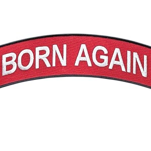 May include: A curved, red embroidered patch with a black border. The text BORN AGAIN is stitched in white capital letters across the center. A yellow cross is positioned on both the left and right sides of the text, completing the design.