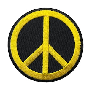 May include: A circular embroidered patch featuring a bright yellow peace symbol centered on a solid black background. The design consists of a thick yellow circular border with a vertical line and two diagonal lines extending from the center.