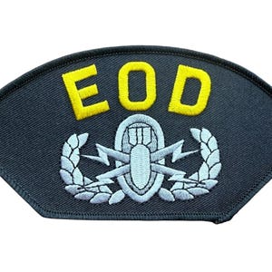 May include: A dark navy blue embroidered patch with a curved top and flat bottom. The text EOD is stitched in bright yellow thread above a light gray emblem featuring a central bomb, two crossed lightning bolts, and a surrounding laurel wreath.