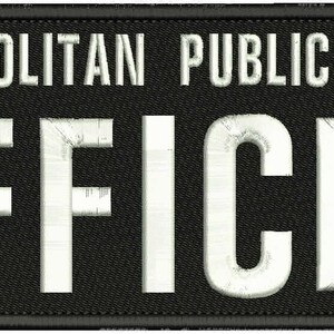 Puede incluir: Un parche rectangular negro bordado con un borde cosido. El texto METROPOLITAN PUBLIC SAFETY está bordado en letras mayúsculas blancas en la parte superior, con la palabra OFFICER en letras mayúsculas blancas grandes centrada debajo.
